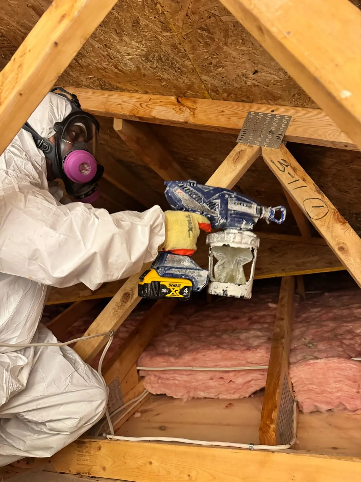 Technician in a protective suit spraying attic sheathing