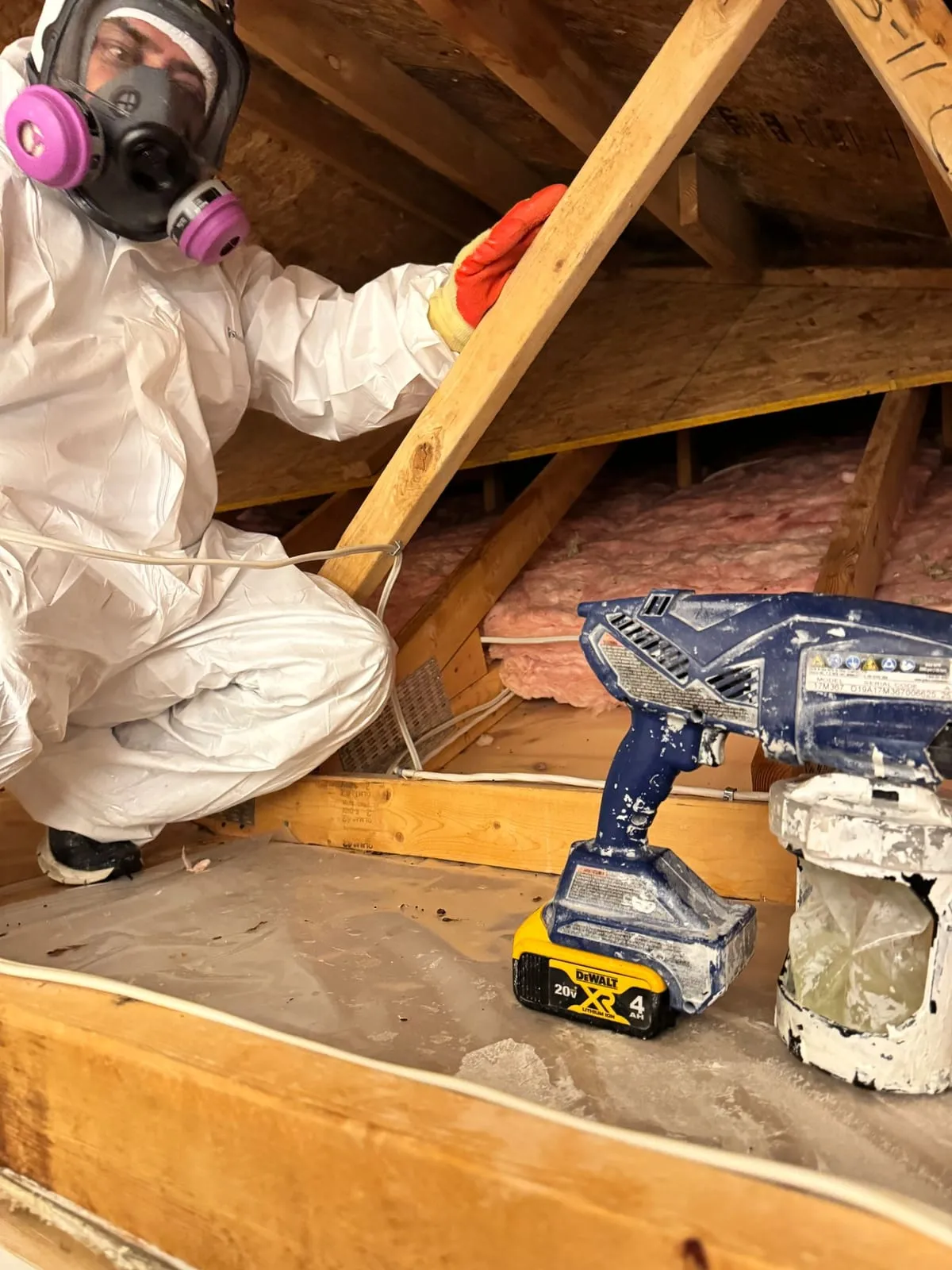 Technician in a protective suit and respirator during attic mold treatment